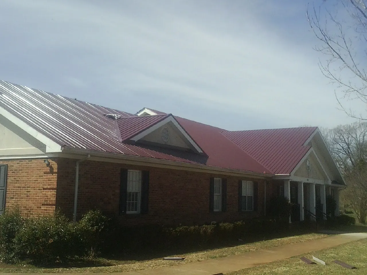 Red metal roof with gabled entries on a long brick building, from a Hail Damage Roof Repair job in Kila