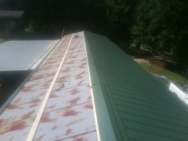 Old rusted panels beside newly installed green metal roofing — Wind Damage Roof Repair by Roofing Brothers in Kila