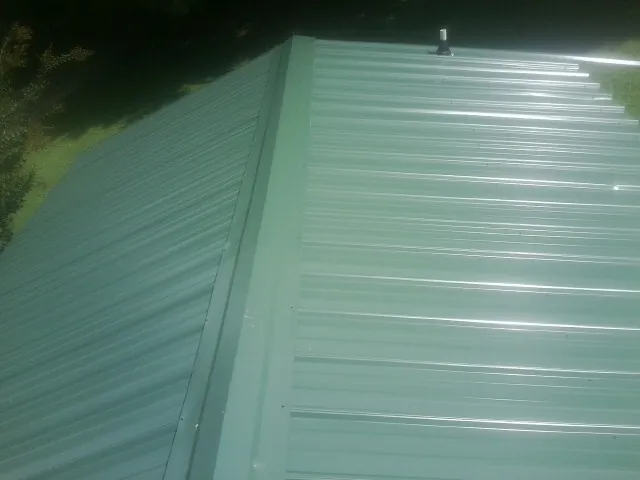 New green metal panels meeting at the ridge of a roof — Flat Roof Repair work by our crew in Kila