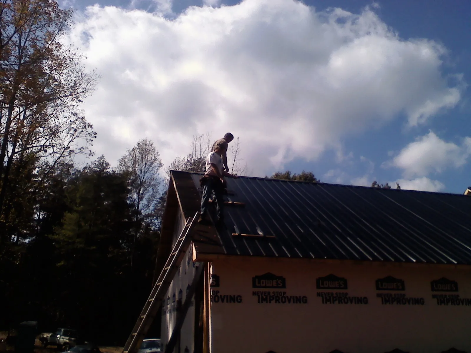 Roofer fastening dark metal panels high against a cloudy sky, from a Roof Inspection job in Kila